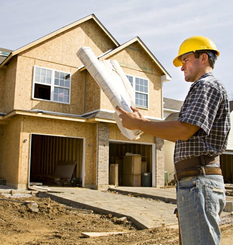 Man with Blueprints outside House Construction Site A construction worker in a hard hat reviewing blueprints in front of a house under construction.