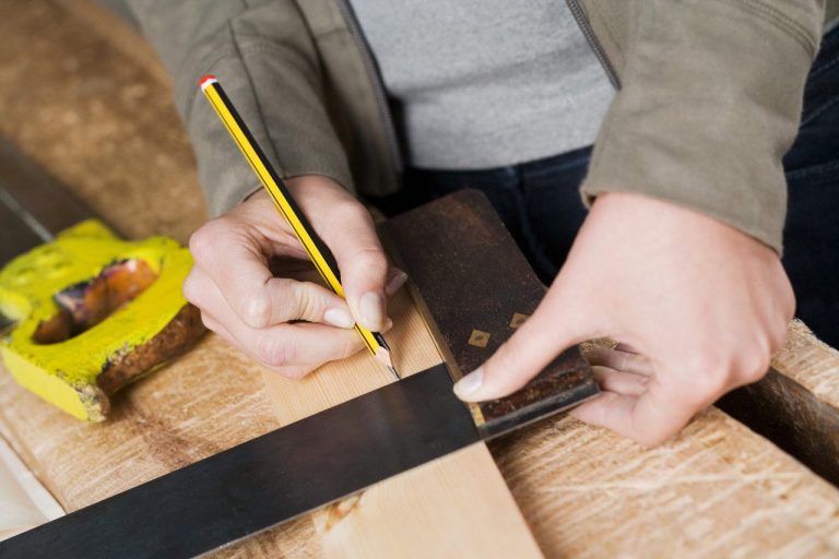 Contractor Hand marking exact measurement and details Person measuring and marking wood with a pencil and square tool on a workbench.