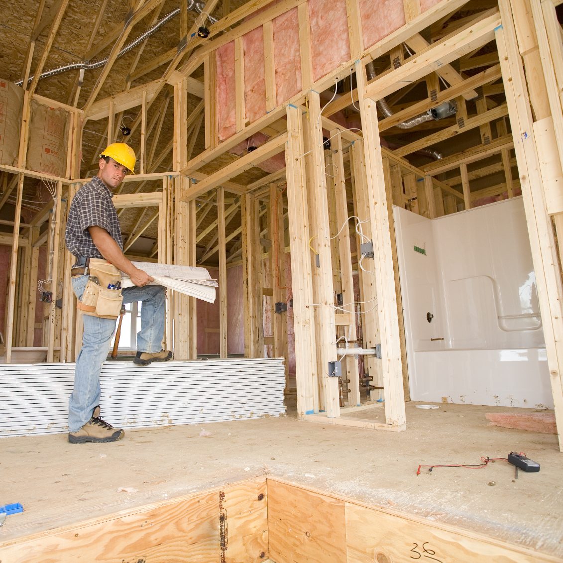 Construction Work Reviewing Blueprint Plans Construction worker reviewing blueprint plans in a partially framed interior space.
